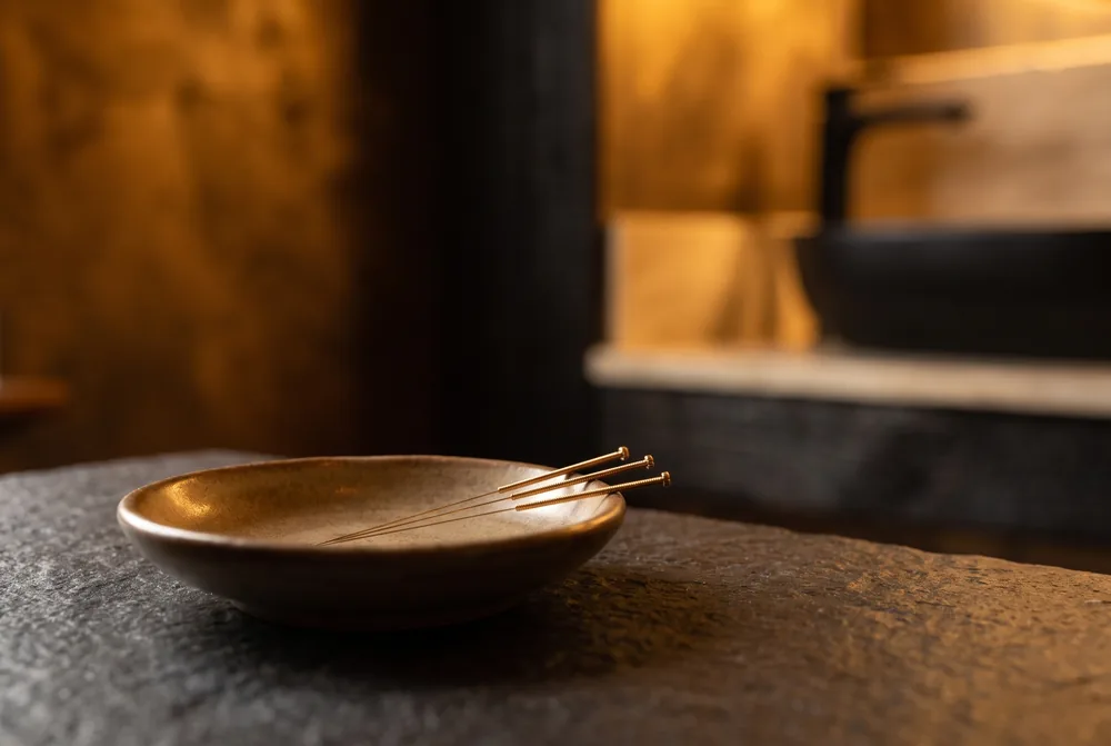 Gold acupuncture needles in a small ceramic dish.