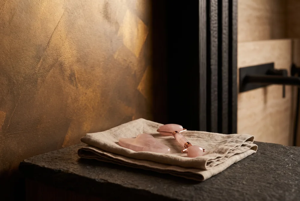 Rose quartz gua sha and roller on folded linen.