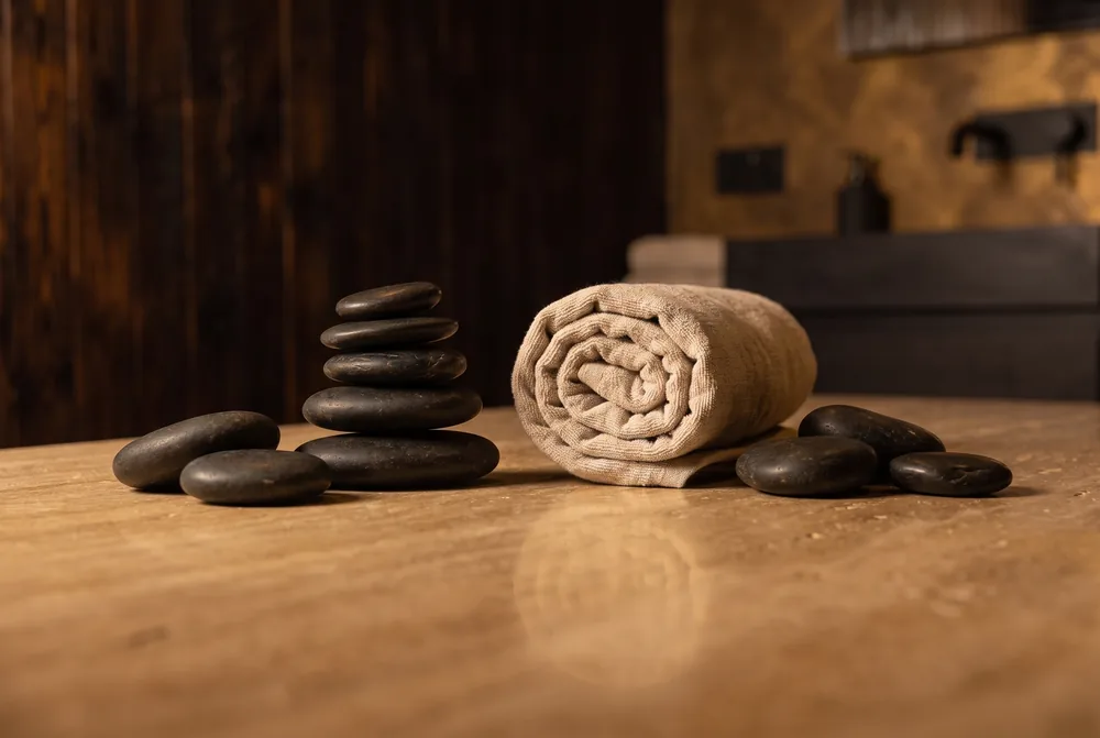 Stacked river stones and a rolled linen towel on warm stone.
