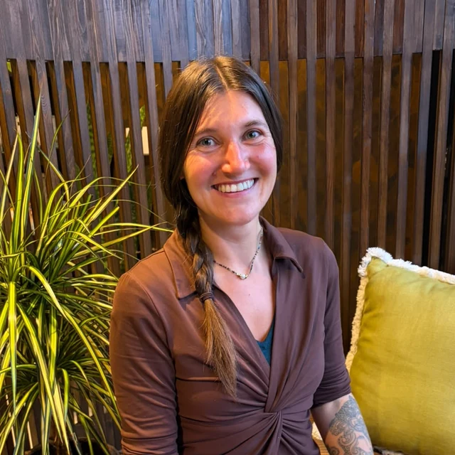 Amy, therapist at Health Pod Frodsham, sitting on a timber bench beside a potted plant